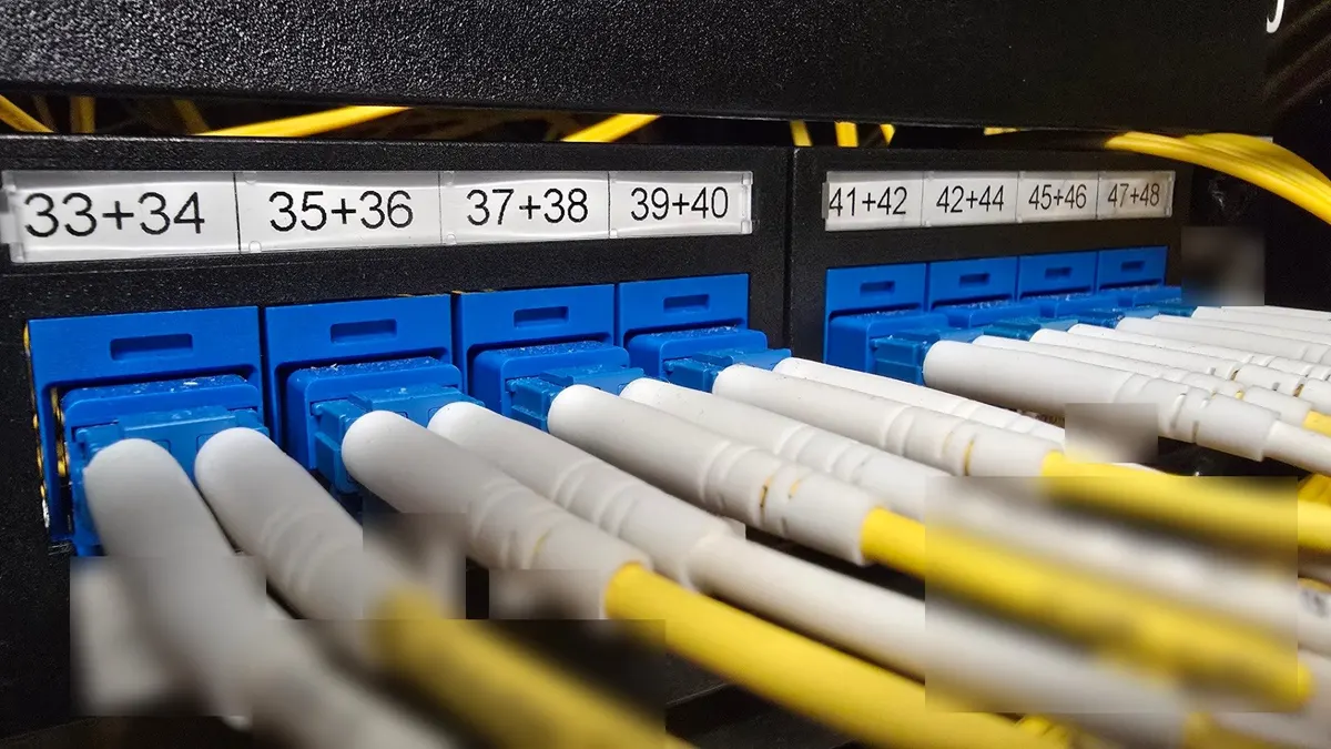 Fibre patch panel with blue adapters and yellow single mode leads, labels blurred